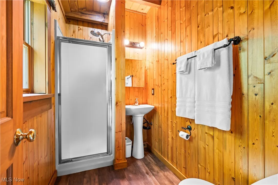 Full bath with wooden walls, a stall shower, wood finished floors, and wooden ceiling