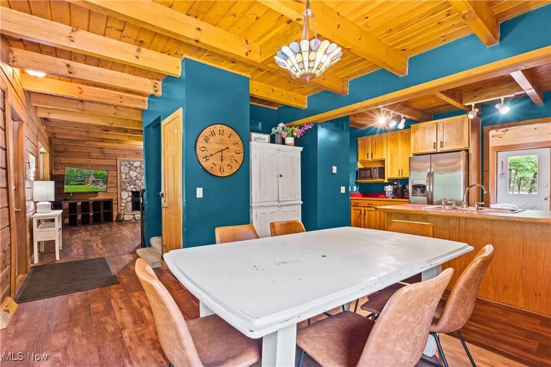 Dining area featuring a wooden ceiling with exposed beams, dark wood-style flooring, wooden walls, a chandelier, and a fireplace
