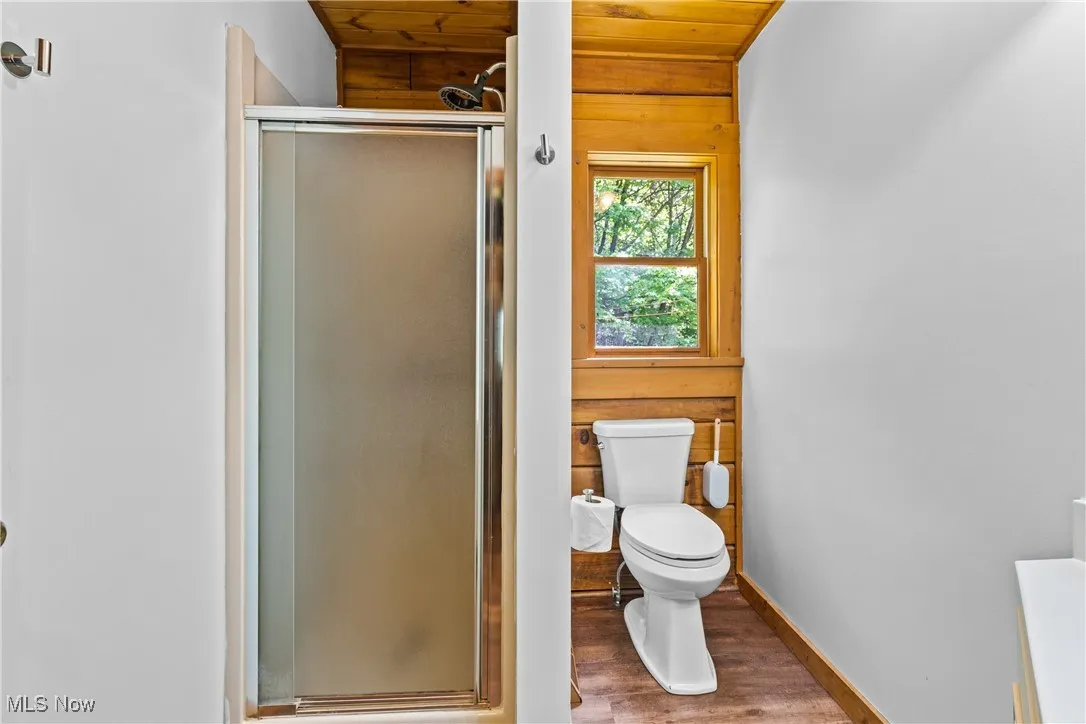 Full bathroom featuring wood finished floors, a shower stall, wooden walls, and wooden ceiling