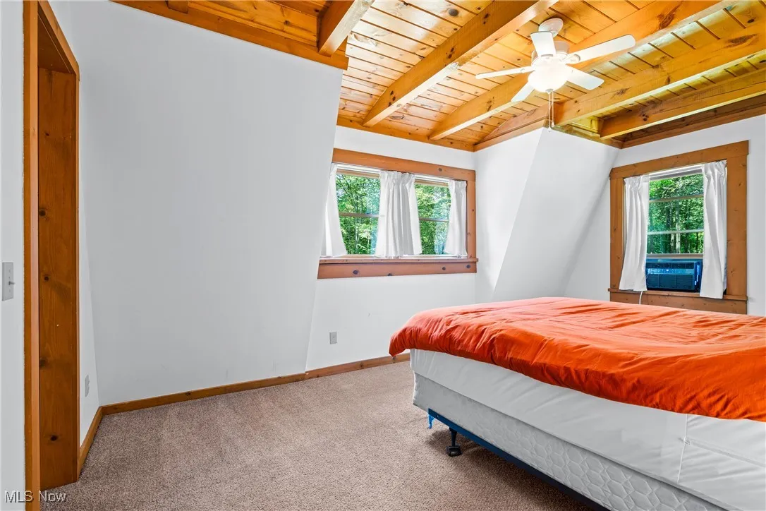 Bedroom with a wooden ceiling with exposed beams, multiple windows, and carpet floors