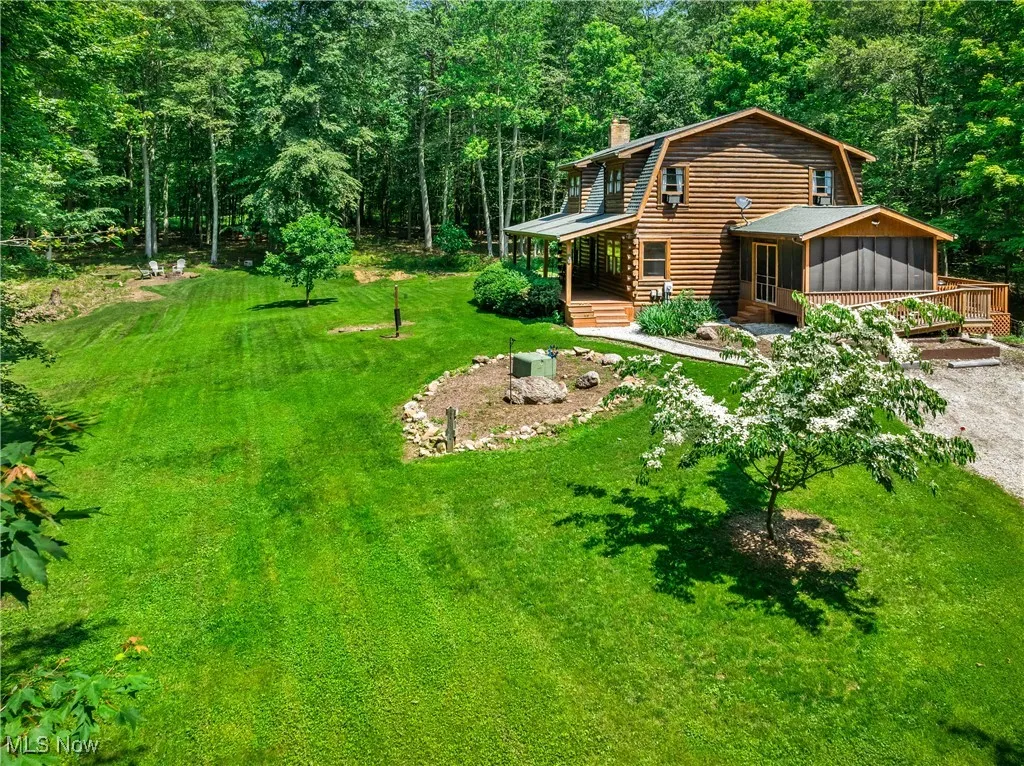 View of green lawn featuring a sunroom, gravel driveway, a wooded view, and a deck