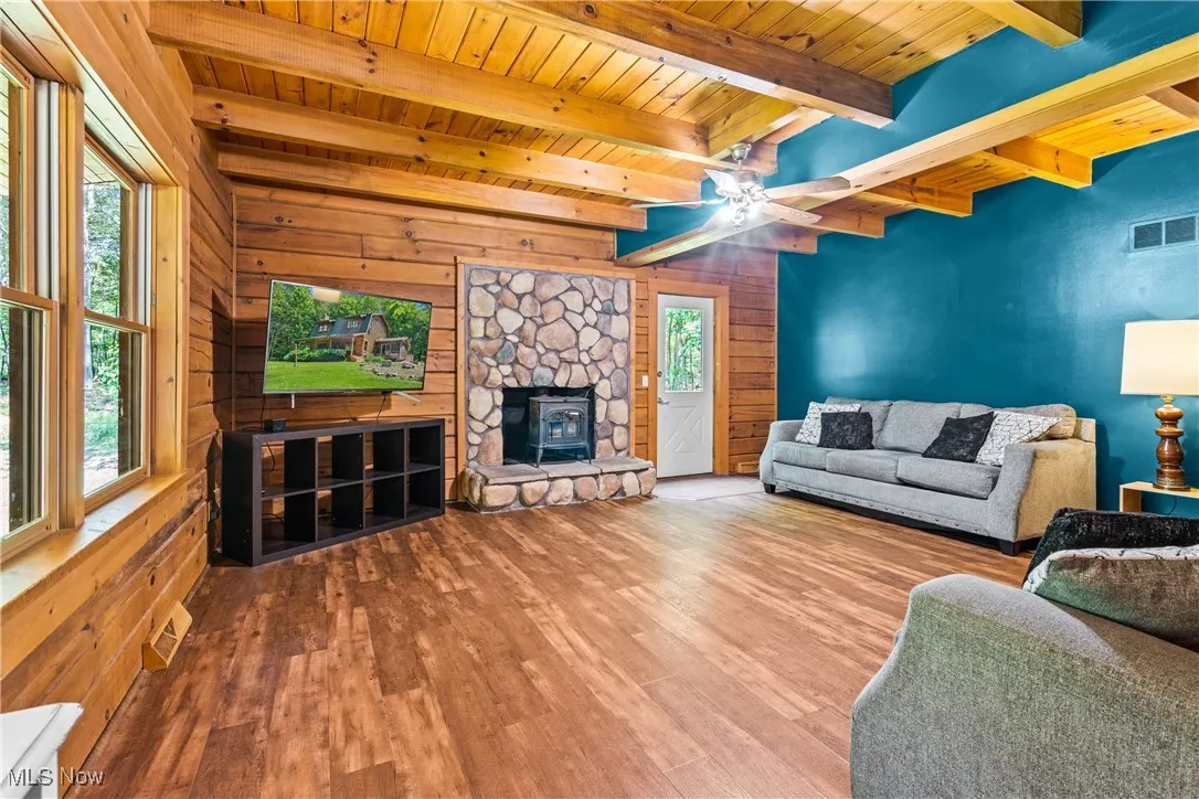 Living area featuring a wood ceiling with exposed beams, wood finished floors, wood walls, and a ceiling fan
