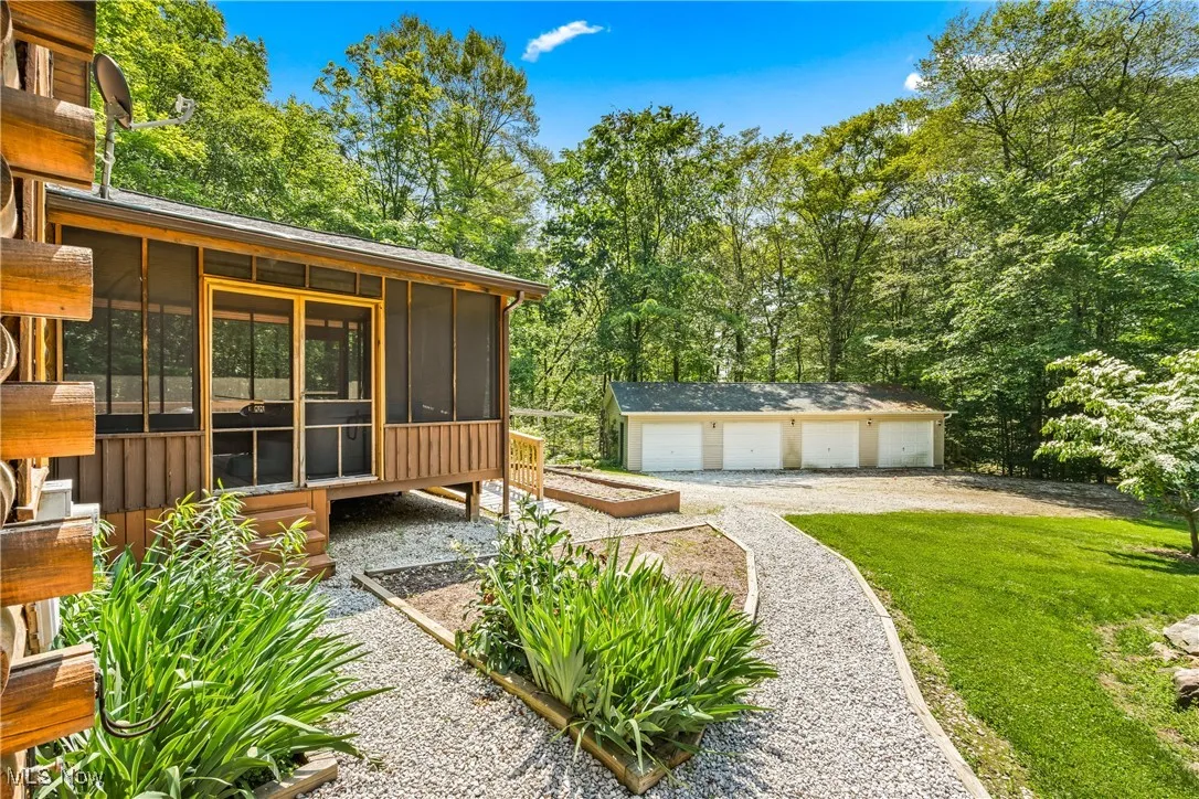 View of grassy yard featuring a sunroom, a detached garage, and an outbuilding