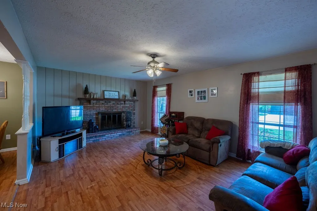Living area with a textured ceiling, wood finished floors, ceiling fan, and a fireplace