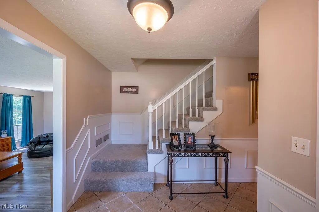 Stairway featuring a textured ceiling, a decorative wall, and a wainscoted wall