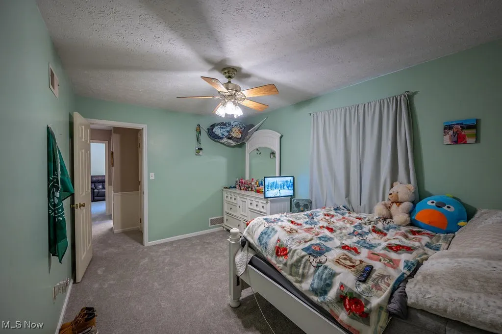 Carpeted bedroom with a ceiling fan and a textured ceiling