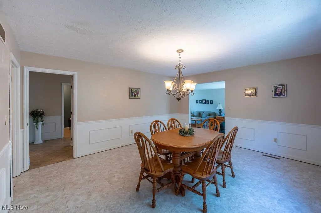 Dining room with a chandelier, a wainscoted wall, a textured ceiling, and a decorative wall