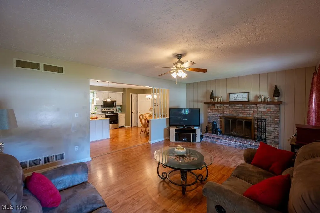 Living area with a textured ceiling, a ceiling fan, light wood-type flooring, and a brick fireplace