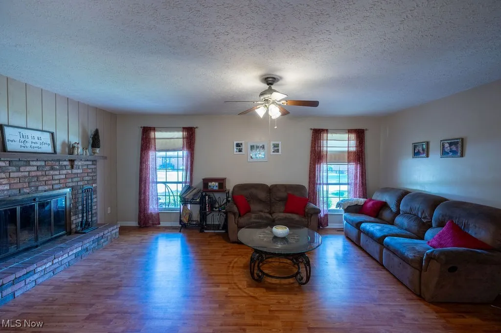 Living area featuring wood finished floors, a textured ceiling, a ceiling fan, and a brick fireplace