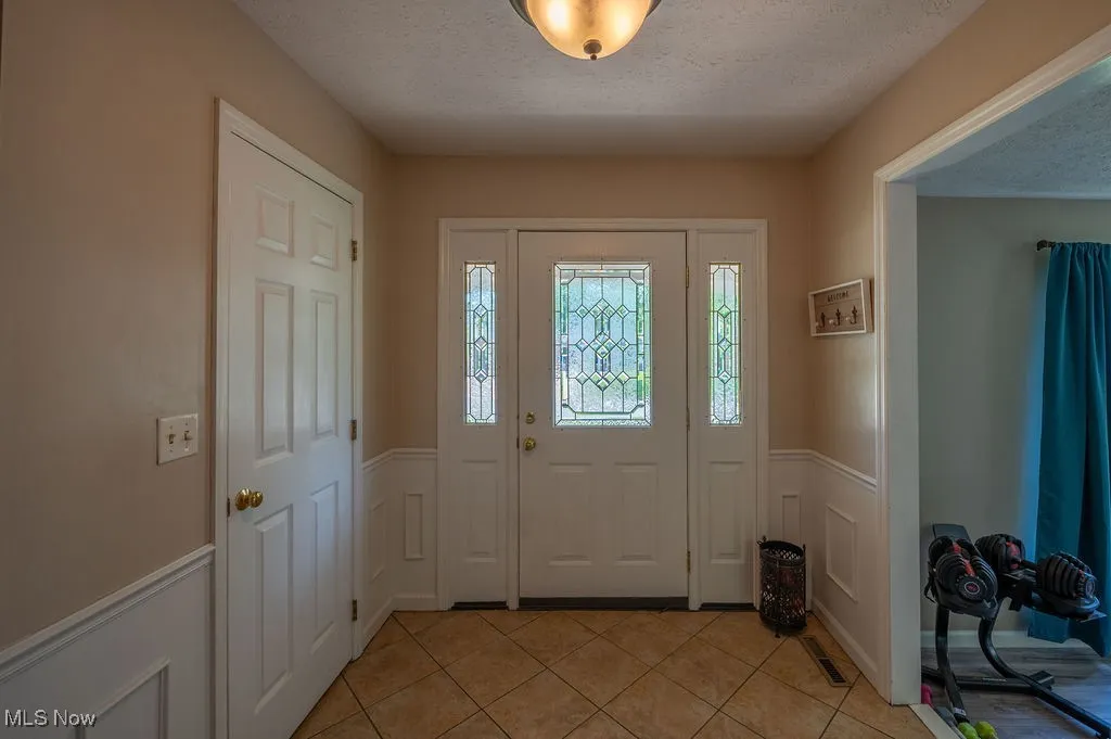 Entryway featuring wainscoting, a textured ceiling, light tile patterned floors, and a decorative wall
