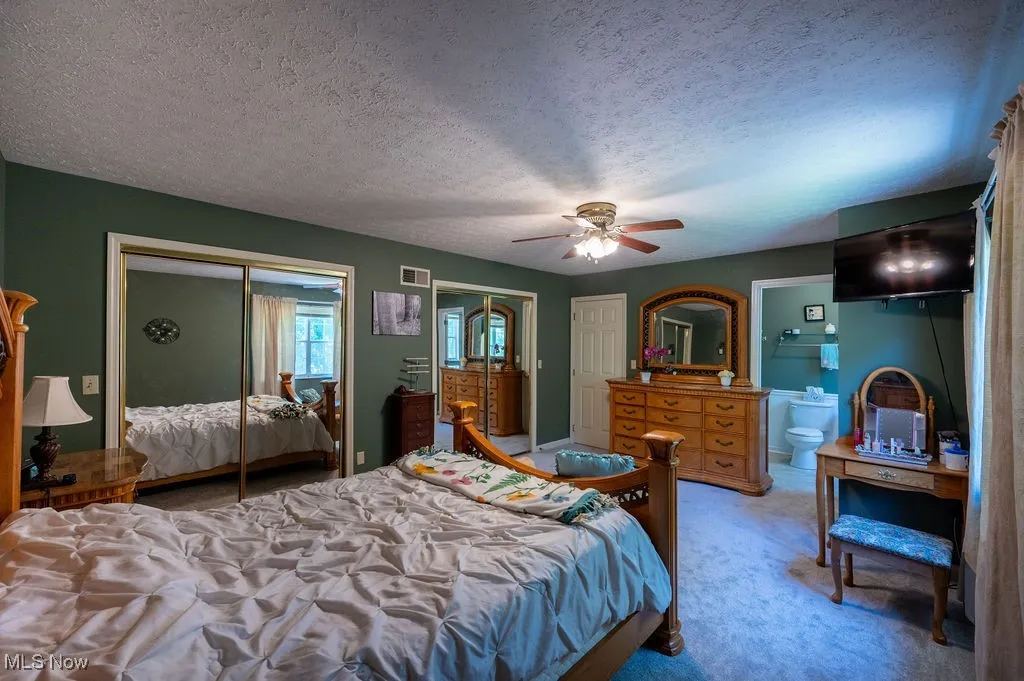 Bedroom featuring two closets, light carpet, a textured ceiling, ceiling fan, and ensuite bathroom