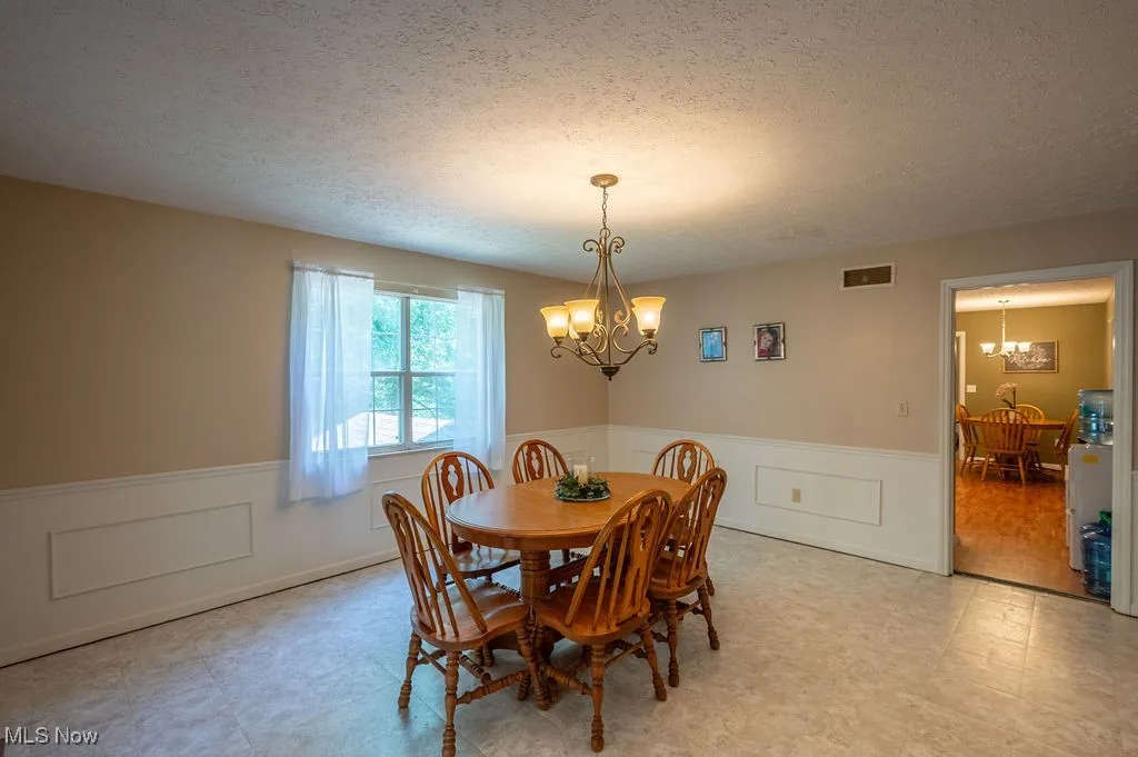 Dining room featuring a chandelier, light floors, a wainscoted wall, and a textured ceiling