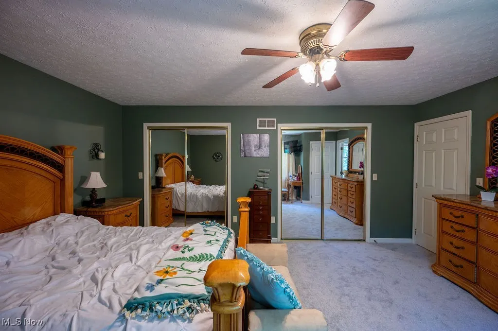 Bedroom featuring multiple closets, a textured ceiling, light carpet, and a ceiling fan