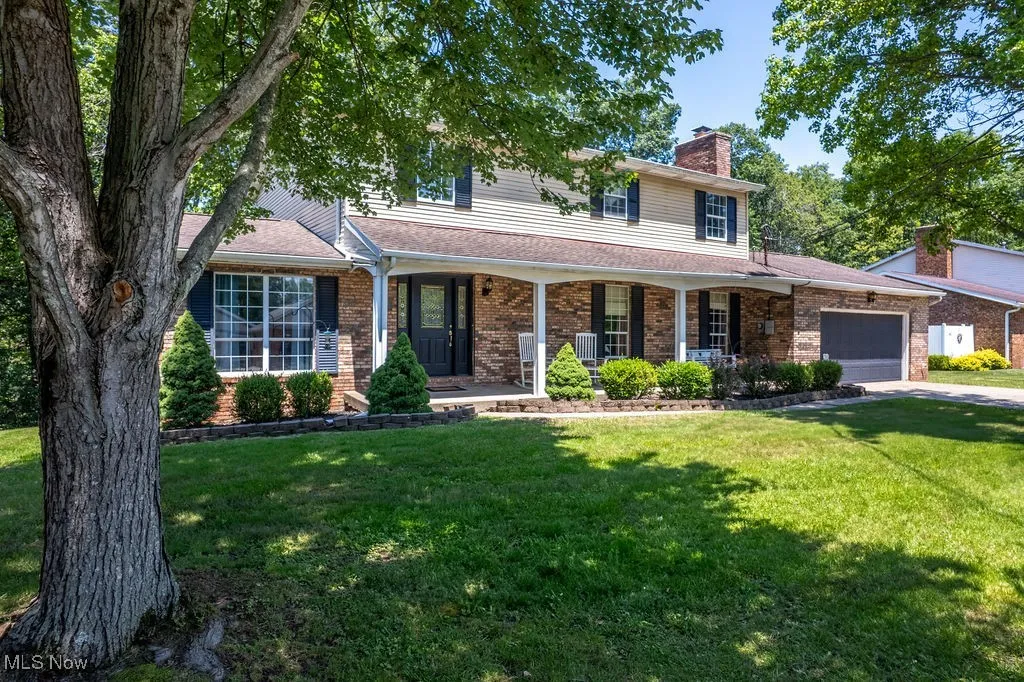View of front facade featuring an attached garage, brick siding, a chimney, a front yard, and covered porch