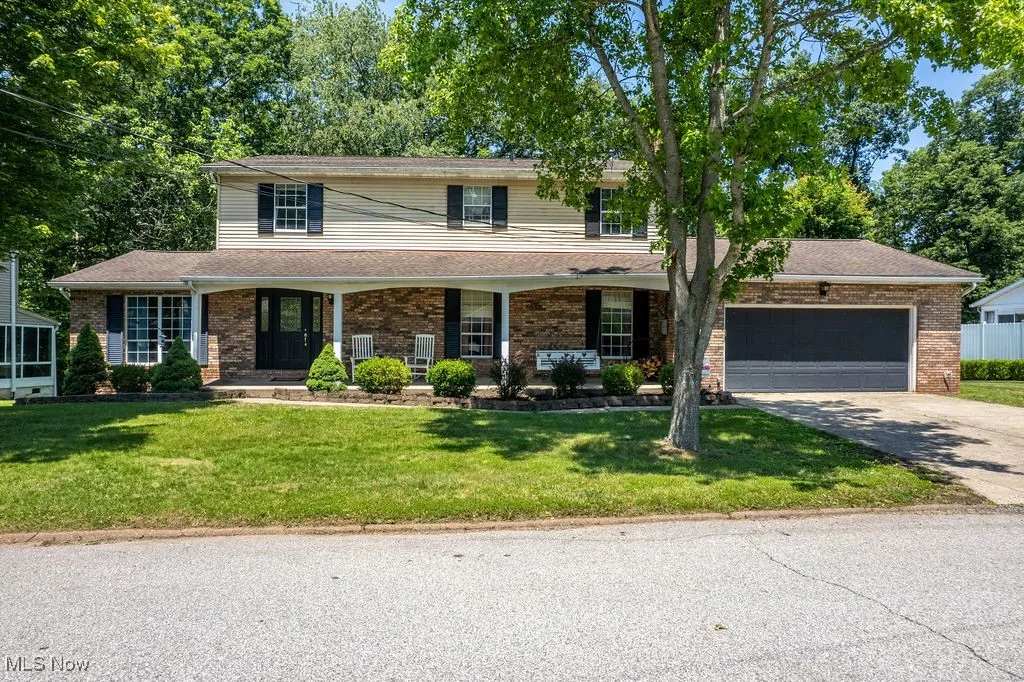 Traditional home featuring driveway, a garage, a front lawn, brick siding, and covered porch