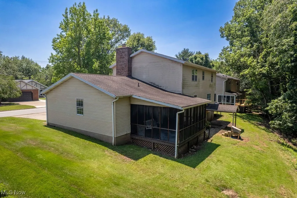 View of home's exterior with a sunroom, a chimney, a shingled roof, and a lawn