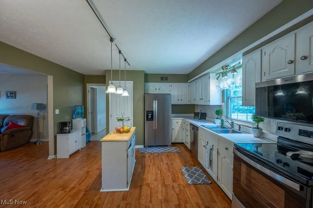 Kitchen with stainless steel appliances, wood counters, white cabinets, light wood-style floors, and a chandelier