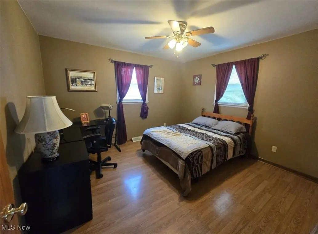 Bedroom featuring multiple windows, light wood-style floors, ceiling fan, and a desk