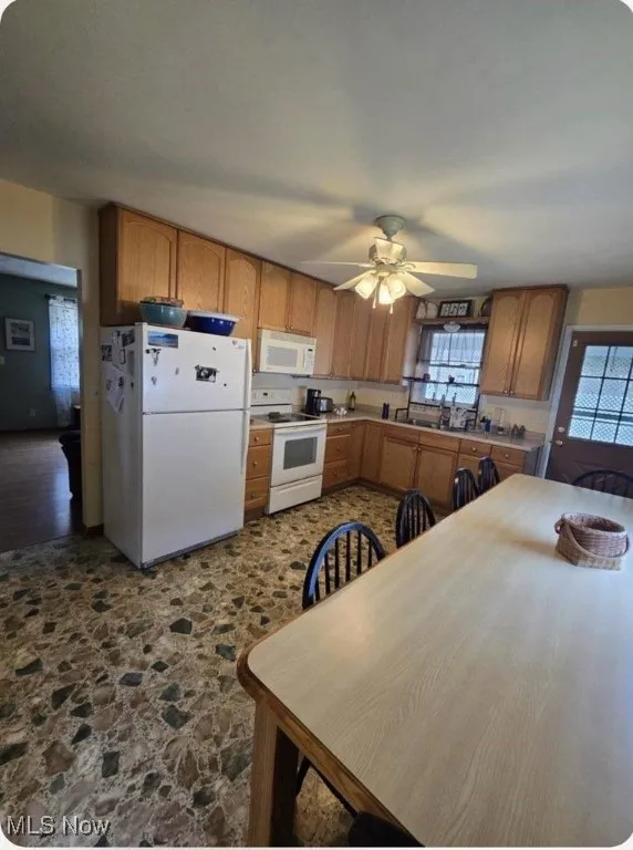 Kitchen with white appliances, stone flooring, and a ceiling fan
