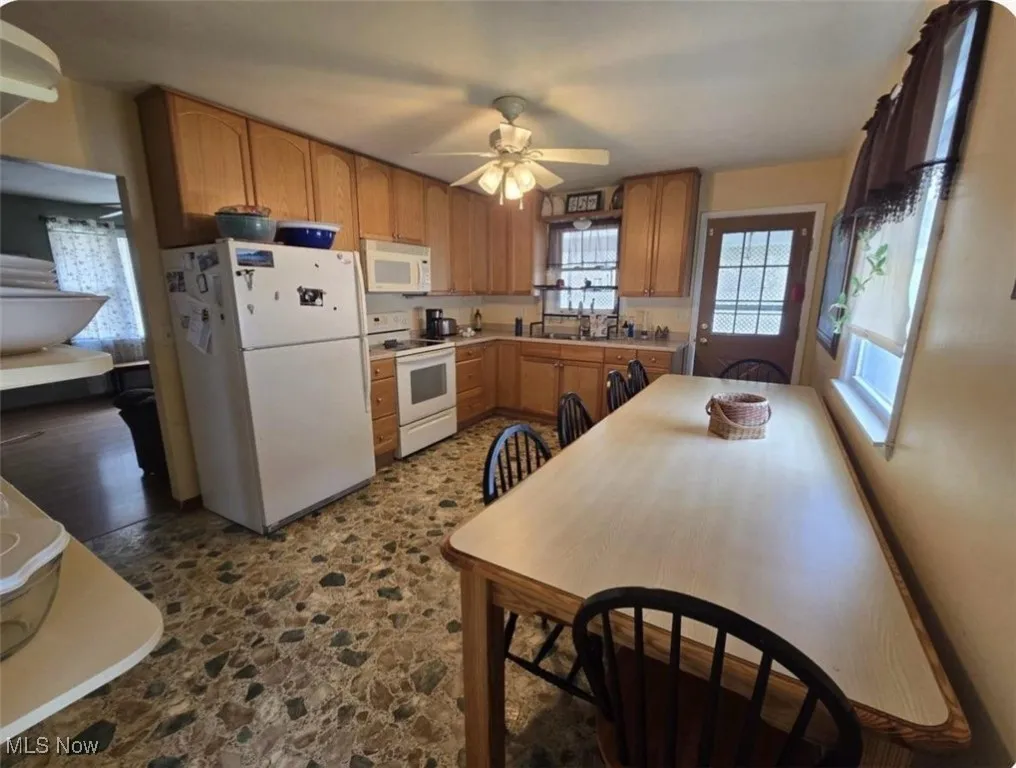 Kitchen with white appliances, dark stone finish floors, a ceiling fan, and light countertops