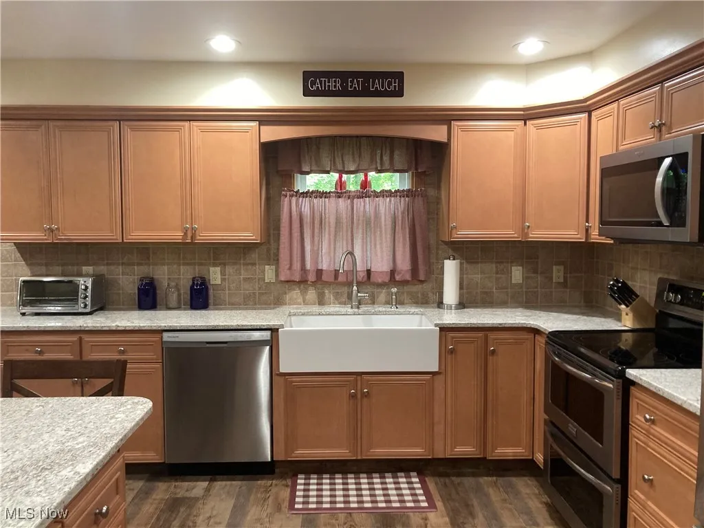 Kitchen with appliances with stainless steel finishes, dark wood finished floors, tasteful backsplash, and brown cabinetry