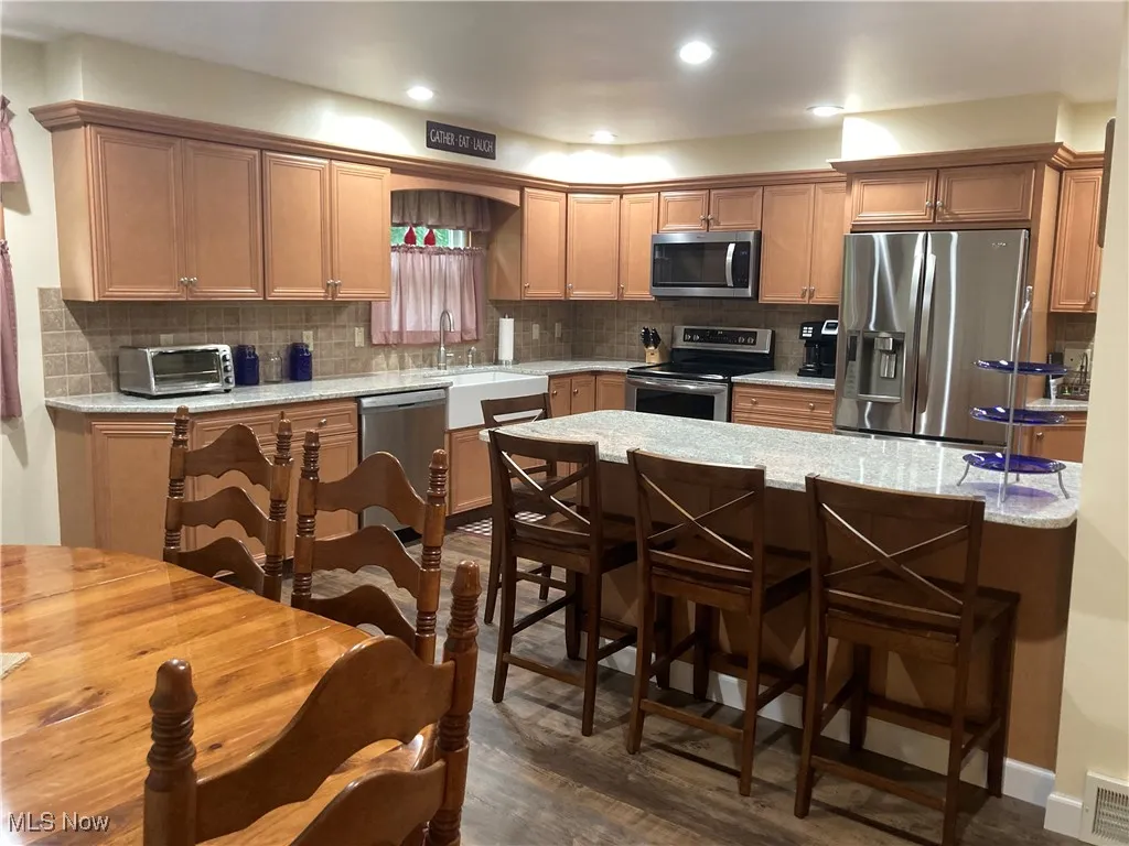 Kitchen featuring stainless steel appliances, a kitchen bar, dark wood-style floors, backsplash, and recessed lighting