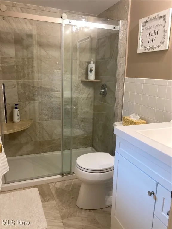 Bathroom with vanity, a shower stall, and tile walls