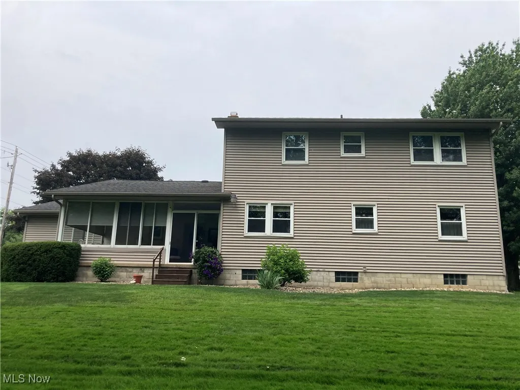 Back of property with a lawn and a sunroom