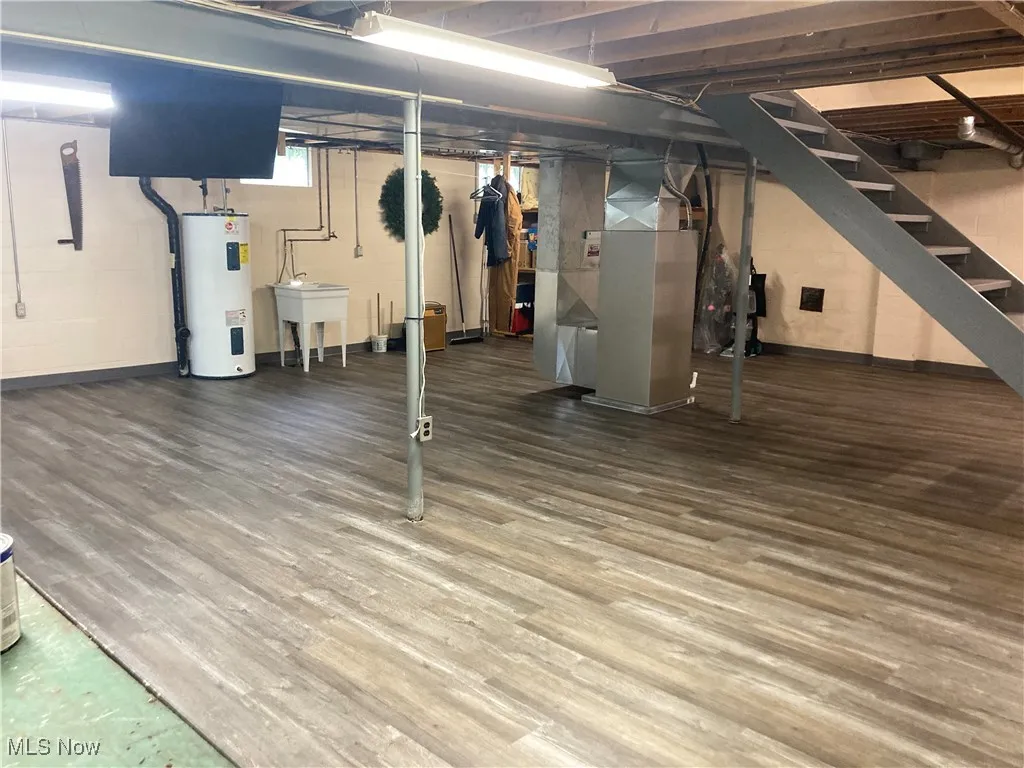 Below grade area featuring water heater, stairway, heating unit, and wood finished floors