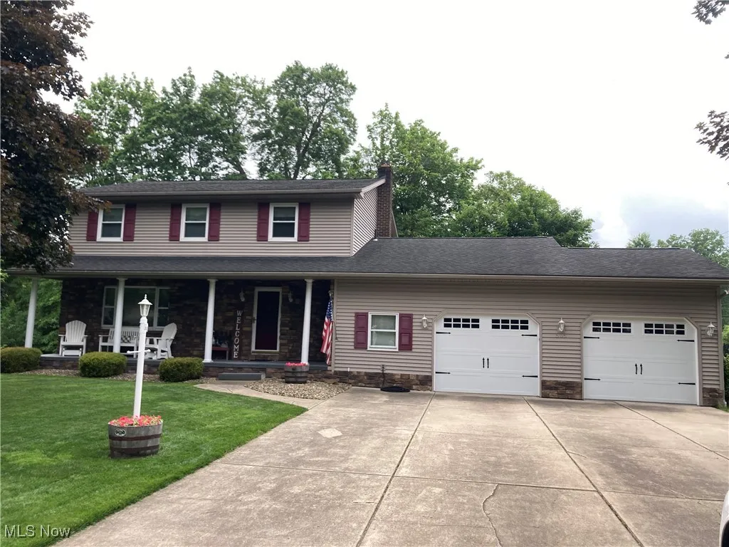 View of front of home featuring a garage, driveway, a front yard, a porch, and stone siding
