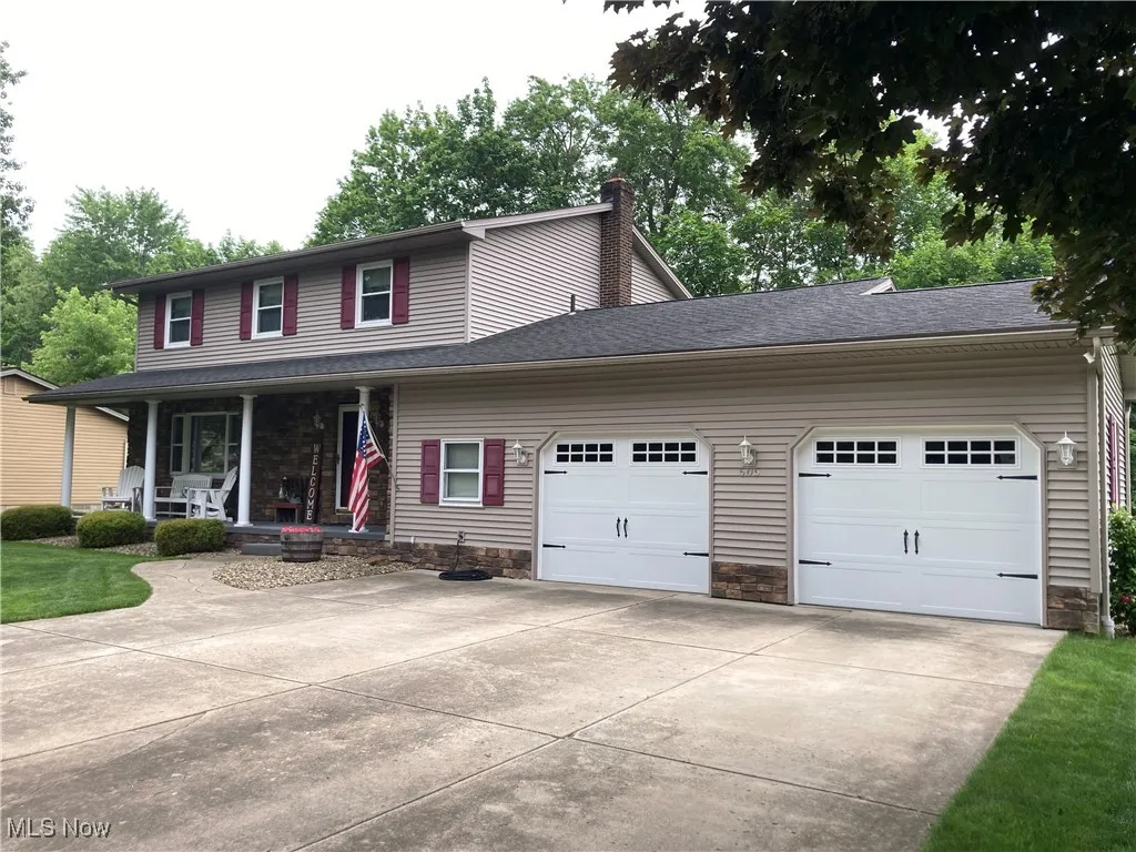View of front of house featuring a porch, driveway, a garage, a chimney, and stone siding