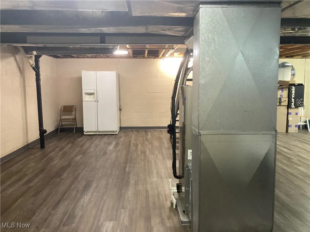 Unfinished below grade area with white fridge with ice dispenser and dark wood-style flooring