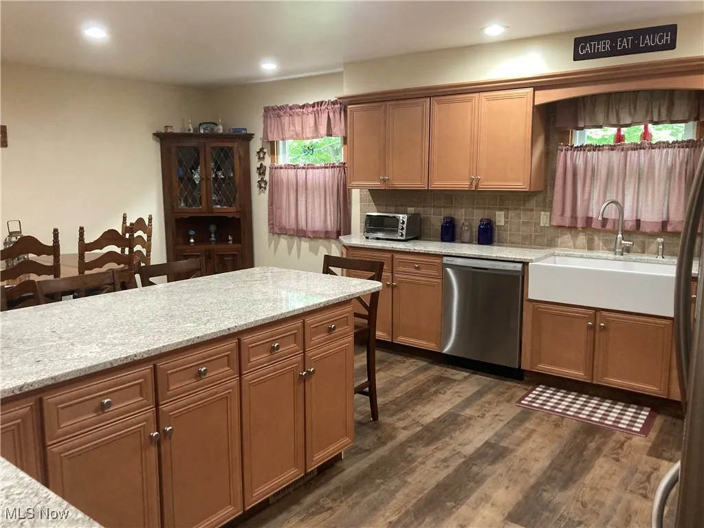 Kitchen with stainless steel dishwasher, dark wood-style floors, backsplash, a kitchen breakfast bar, and brown cabinetry
