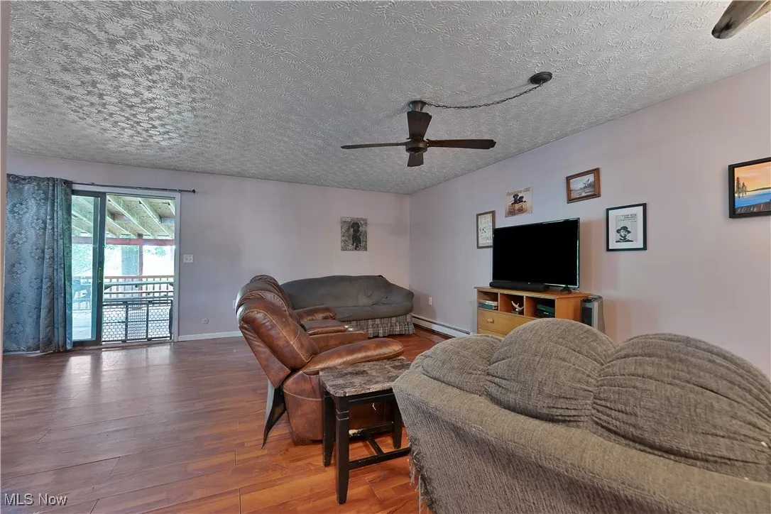 Living room featuring a textured ceiling, ceiling fan, wood finished floors, and baseboard heating