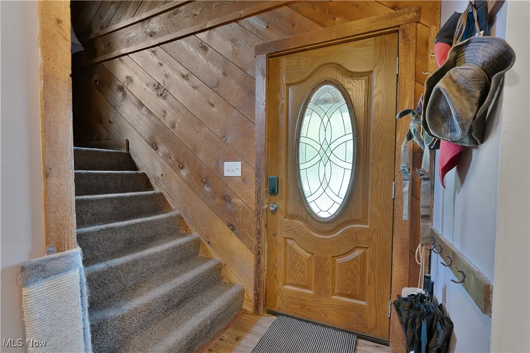 Foyer entrance featuring wooden walls, stairway, and light wood-style floors