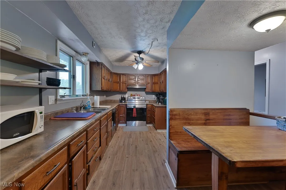 Kitchen featuring stainless steel range with electric cooktop, white microwave, light wood finished floors, open shelves, and ceiling fan