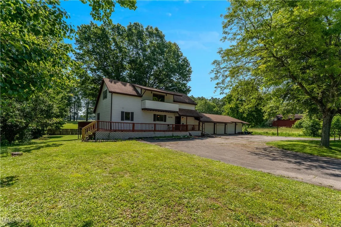 View of front of house featuring driveway, a front yard, a wooden deck, and a garage