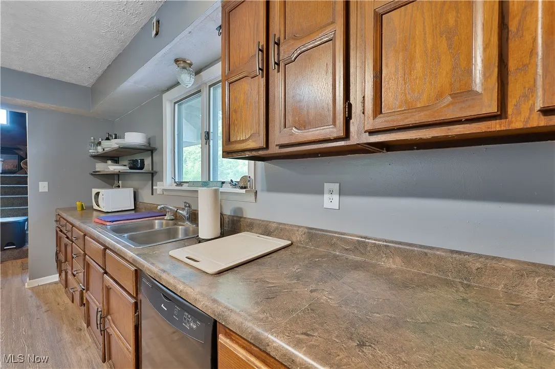 Kitchen featuring white microwave, dishwashing machine, brown cabinetry, light wood-style flooring, and open shelves
