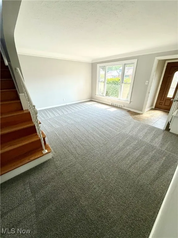 Unfurnished living room with carpet floors, stairs, and crown molding