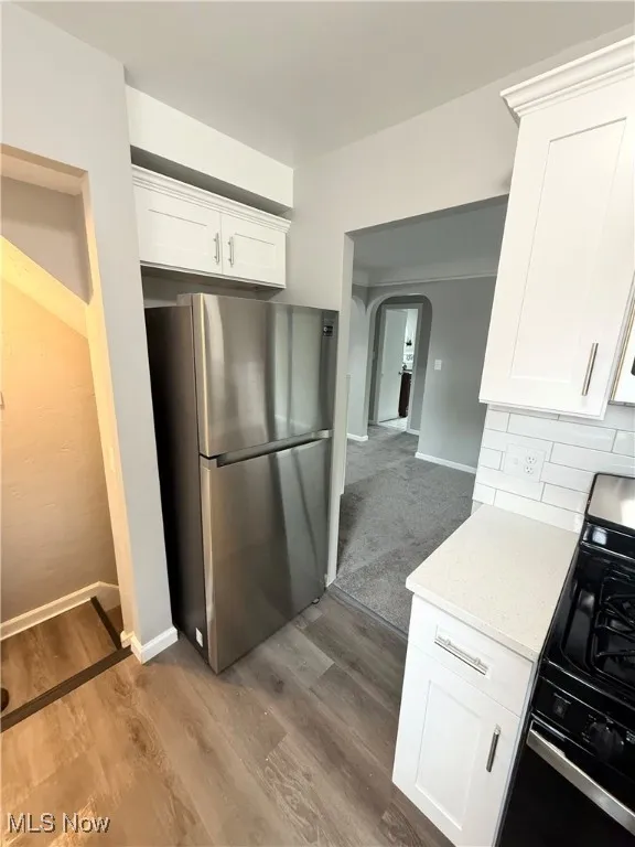 Kitchen featuring freestanding refrigerator, range with gas stovetop, arched walkways, dark wood-style floors, and white cabinets