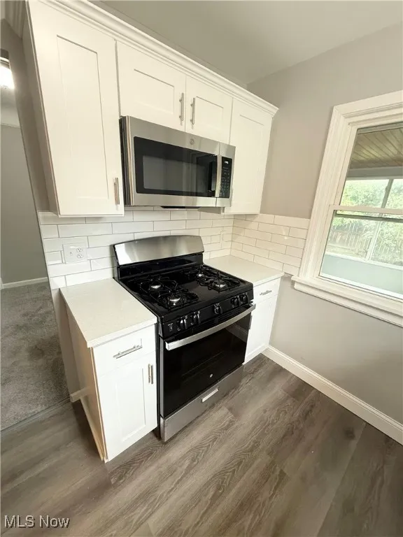 Kitchen featuring stainless steel appliances, light countertops, dark wood-style flooring, and white cabinetry