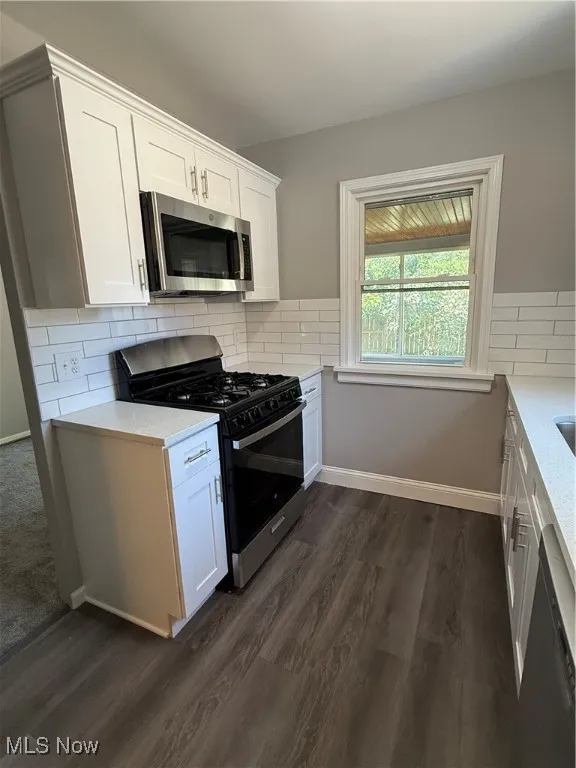Kitchen with stove, dark wood-type flooring, white cabinetry, backsplash, and dishwashing machine