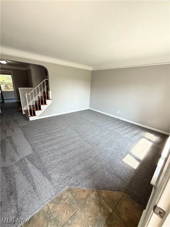 Empty room featuring dark colored carpet, a textured ceiling, stairway, and ornamental molding