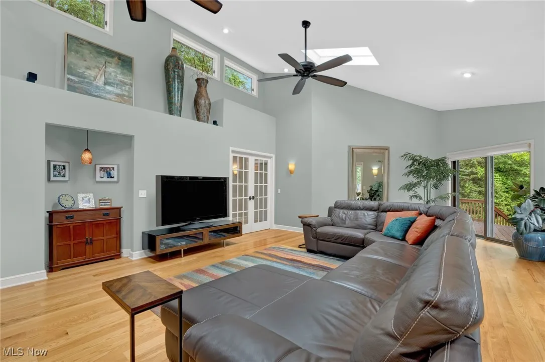 Light-filled great room with newer wide-plank ash hardwood flooring, 2 ceiling fans, 3 skylights, wall of windows, recessed lighting, access to deck. Private wooded views.