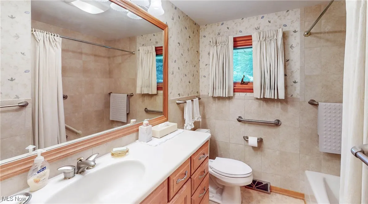 Full bath featuring tile walls, wallpapered walls, vanity, and a wainscoted wall