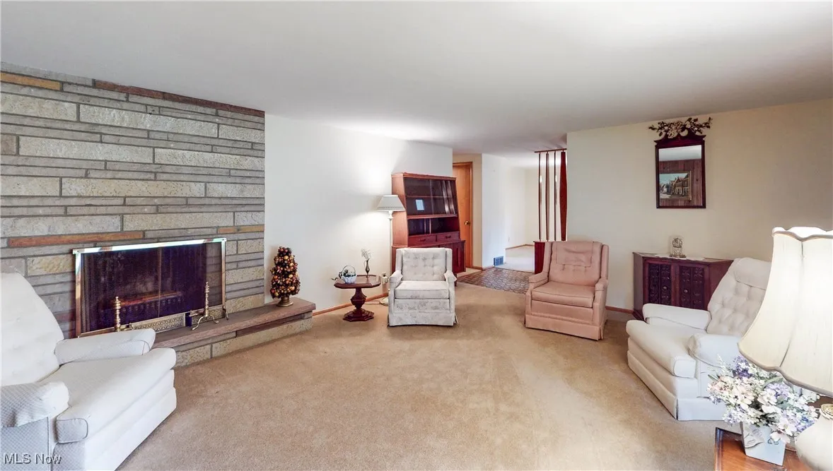 Carpeted living room featuring a stone fireplace and baseboards