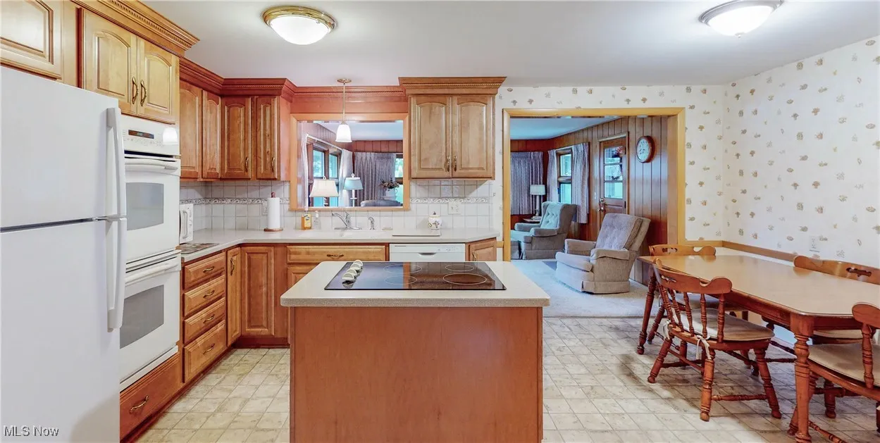 Kitchen with white appliances, light flooring, a center island, light countertops, and wallpapered walls