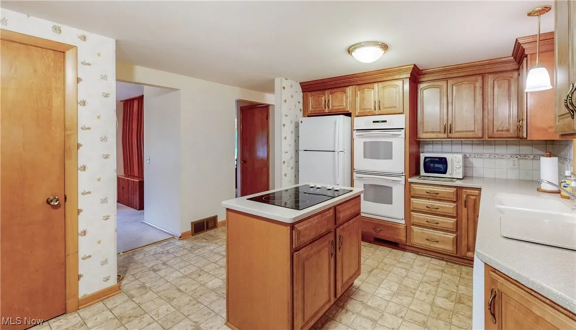 Kitchen featuring white appliances, a kitchen island, light countertops, and light flooring