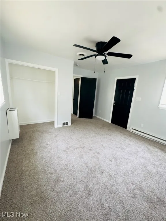 Unfurnished bedroom featuring a baseboard heating unit, carpet flooring, and a ceiling fan
