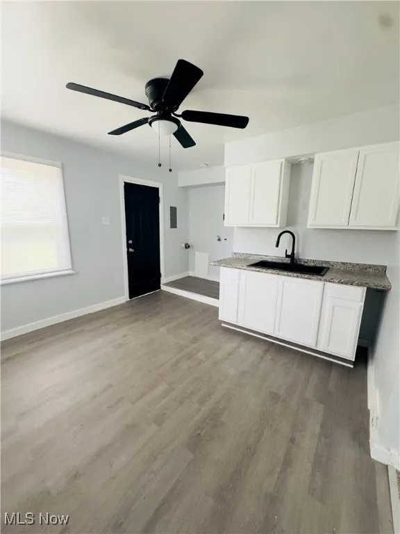 Kitchen with white cabinetry, wood finished floors, ceiling fan, and dark stone counters